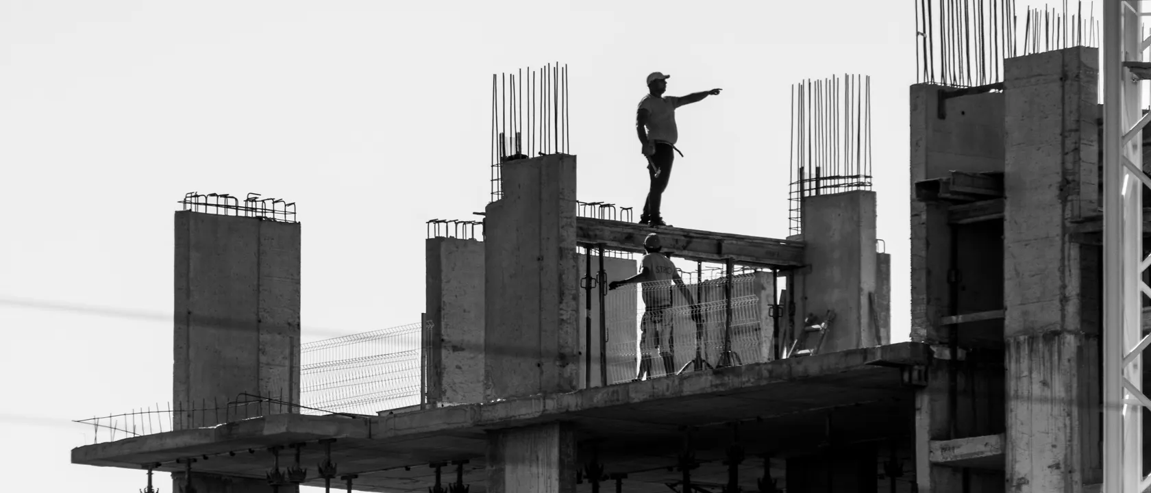 Construction workers silhouetted against the sky on the concrete frame of a building under construction